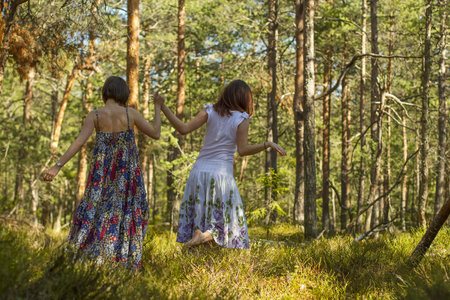 two young women in long dresses  holding each other's hand are roaming through the forest in springtimeの写真素材