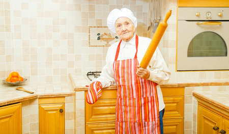 Kind elderly lady holding a rolling pin in the kitchen.の写真素材