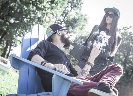 Hipster couple taking a break and smoking on bench.の写真素材