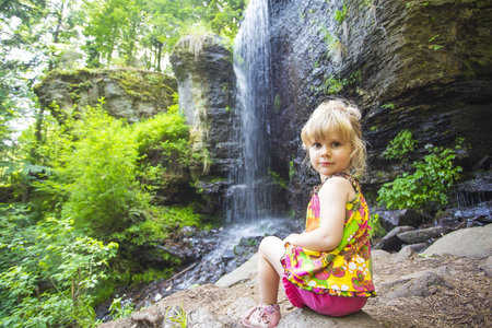 Littlei girl sitting next to idyllic tropical waterfallの写真素材