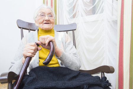 Elderly lady with a walking stick sitting in a chair.の写真素材