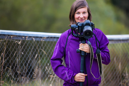 brunette woman standing near the fence with a cameraの写真素材