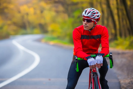 young well equipped man standing with his racing bike by the roadsideの写真素材