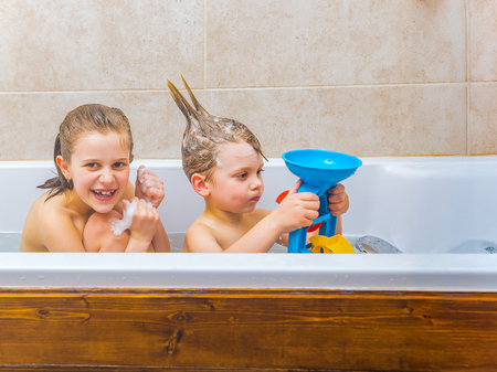 Two children having fun during bath time, playing with toys and foam, creating joyful childhood memories in a cozy home bathroom setting.の写真素材