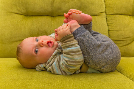 A cute baby lying on a green couch, grabbing their feet playfully, exuding joy and curiosity.の写真素材
