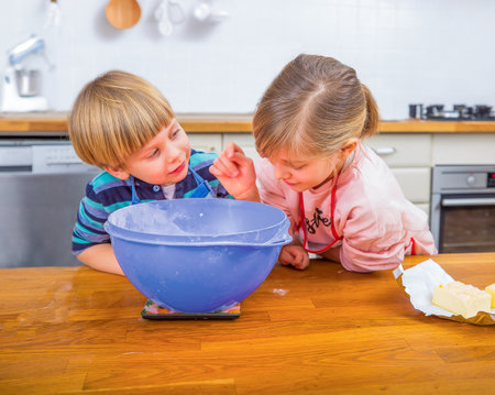 Two children enjoy baking in a bright modern kitchen, measuring ingredients and sharing moments of joy.の写真素材