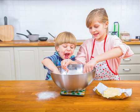 Two young siblings enjoying baking activities together in a kitchen, fostering creativity and family connection with fun expressions and joyful interaction during the culinary preparation.の写真素材