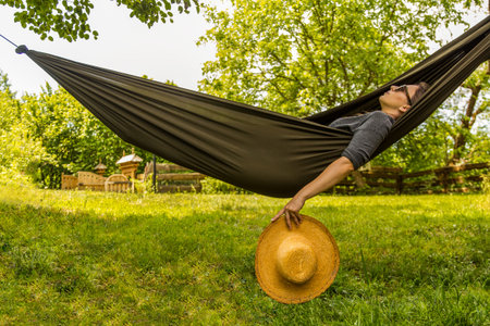 Experience tranquility in a lush green outdoor setting, lying in a hammock with a straw hat.の写真素材
