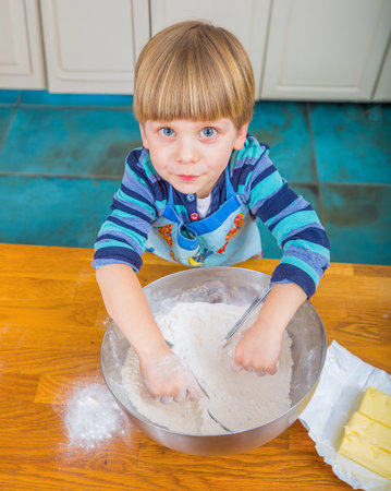 A child in a kitchen cheerfully mixing baking ingredients with concentration and enthusiasm.の写真素材