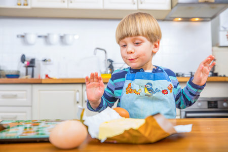 A cheerful young boy in a colorful apron is engaging with baking in a lively kitchen setting. The image captures a moment of concentration and joy in the process of culinary creativity.の写真素材