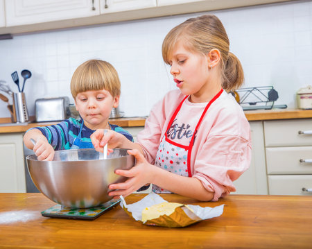 A boy and a girl mix ingredients in a bowl together, engaging in creative baking activities. They are in a bright and family-friendly kitchen setting, enjoying teamwork and culinary experiences.の写真素材