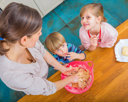 A mother and her children bonding while preparing cookie dough on a wooden countertop. Baking activities like these bring families closer, creating joyful memories and strengthening relationships while enjoying delicious homemade treats.の写真素材