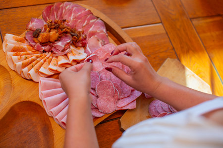 Hands arrange meat slices on a wooden charcuterie board during food preparation.の写真素材