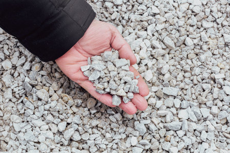 Close-up of a hand holding small gravel stones over a bed of similar rocks.