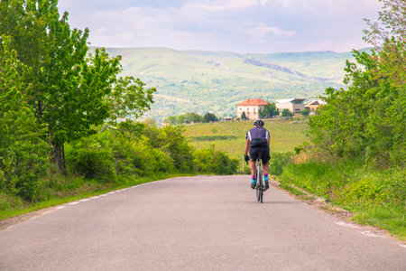 Cyclist riding on a rural road amidst lush greenery and scenic countryside.の写真素材