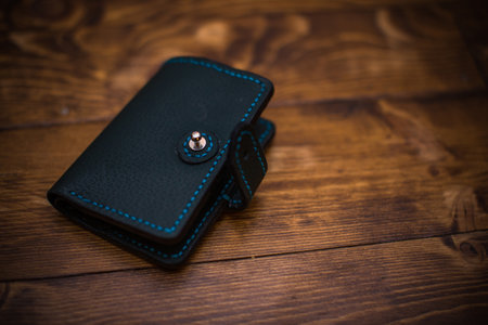 Elegant leather wallet featuring fine blue stitching detail, placed on a wooden background.