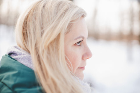 Close-up profile of a blonde woman wearing a green jacket and a light purple scarf, looking to the...