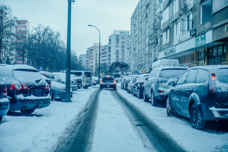 Cars are stuck in traffic on a snow-covered street in a city during winter, with apartment buildings lining the roadの写真素材