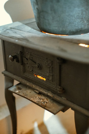 A vintage cast iron wood stove with a pot on top and glowing embers visible through the firebox...