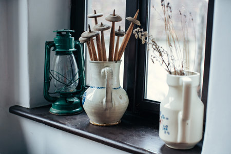 A collection of antique spinning tools and a kerosene lantern are displayed on a windowsill with dried flowersの写真素材