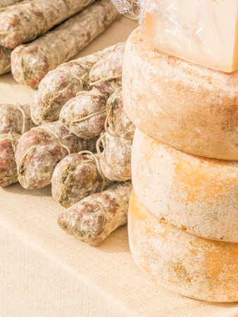 stacked rounded cheese and group of salami on tablecloth for sale in the local marketの写真素材