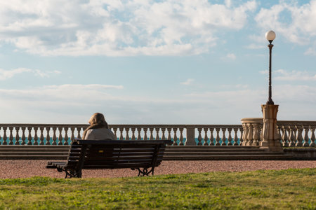 lonely woman sitting on public bench near terrace with sea view, lonelinessの写真素材