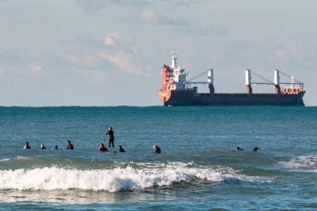 surfers waiting for waves, container ship in backgroundの写真素材