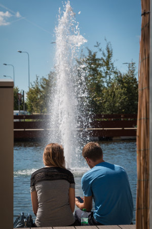 Boy and Girl Having a Seat Near Fountain with Water Spray in Parkの写真素材
