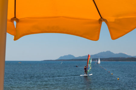 Summer Beach: Yellow Beach Umbrella, WindSurfer, Hills and Sea in backgroundの写真素材