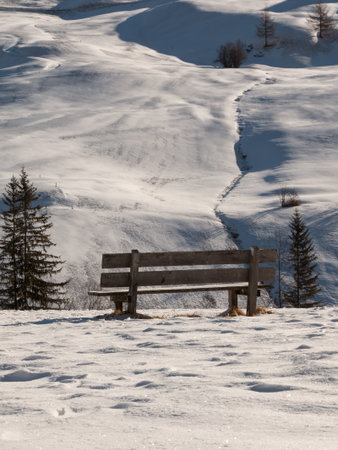 Wooden Bench Among Fresh Snow in Winter Sunny Day in Italian Dolomites Mountains.の写真素材