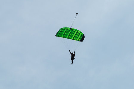 Parachutist with Green Parachute against Blue Sky preparing for Landing