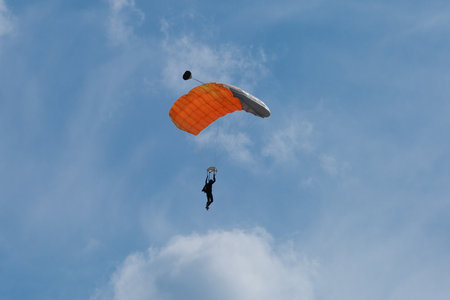 Parachutist with Orange Parachute against Blue Sky preparing for Landingの写真素材