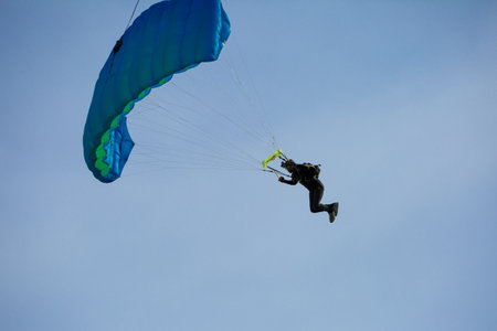 Parachutist with Blue Parachute against Blue Sky preparing for Landingの写真素材