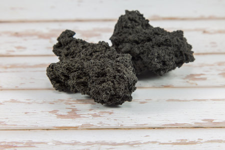 Black Lava Rock from Volcano on White Wooden Plank.の写真素材