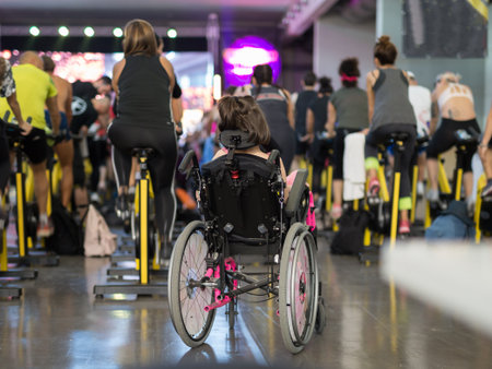 Girl in Pink Wheelchair attending a Fitness Workout with Spinning Bike.の写真素材