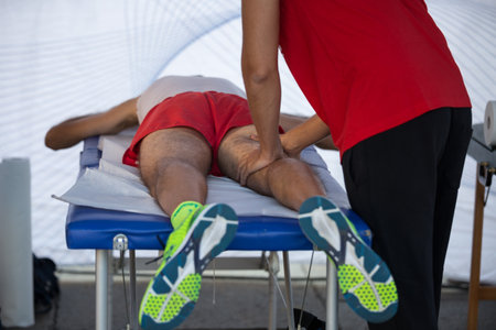 Athlete lying on a Bed while having Legs Massaged after a Physical Sports Workout.の写真素材