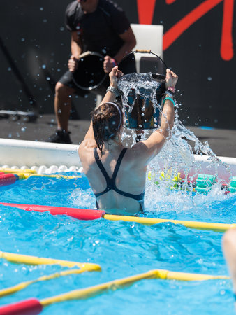 Girl Doing Water Exercises in Outdoor Swimming Pool Emptying a Bucket of Water on her  Head.のeditorial素材