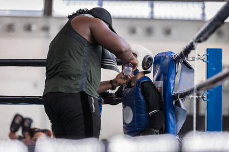 Child Boxer is Quenching in the Ring's Corner during the Break with his Coach.の写真素材