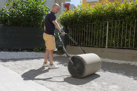Man Dragging the Garden Roller on Gravel and Sand in Garden.