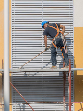 Worker with Blue Hardhat at Work on a Scaffold in a Building Site for the Construction of a Building.の写真素材