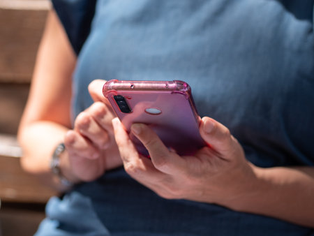 Detail of the Hands of a Woman using her Mobile Phone with Pink Cover.の写真素材