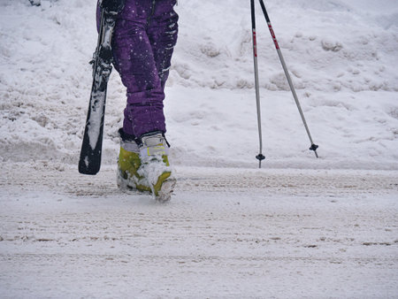 Detail of the Boots and Purple Ski Pants of a Lady's Ski Suit Walking on the Snowy Road Returning...