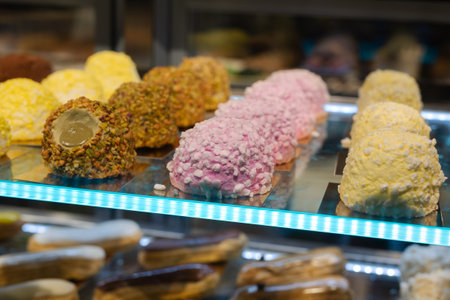 Pink, Yellow and Brown Pastries filled with Hazelnut and other Flavors and displayed on a Glass Shelf in a Pastry Shop.の写真素材