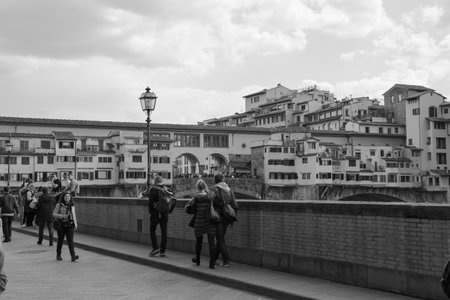 Tourists strolling along the Arno River and View of the crowded Ponte Vecchio on a Beautiful Sunny Spring Day in Florence, Italy.の写真素材