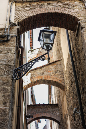 An Antique Lamp Post in a Narrow Street with Ancient Walls and Arches in Italy.の写真素材