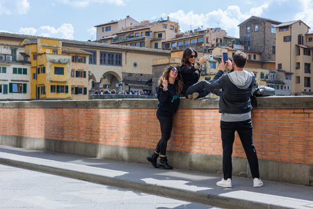Tourists strolling along the Arno River and View of the crowded Ponte Vecchio on a Beautiful Sunny Spring Day in Florence, Italy.の写真素材