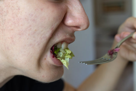 Detail of a Boy's Mouth Biting Salad Leaves.の写真素材