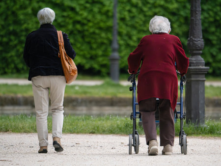 Two Elderly Ladies Walking in a Public Park, one with the aid of a Walkerの写真素材