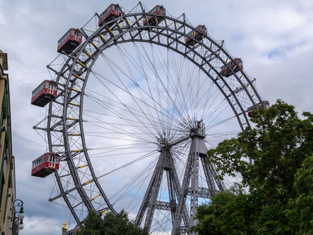 Historic Vienna Ferris Wheel with Classic Red Cabins Against a Cloudy Sky, Austria.の写真素材