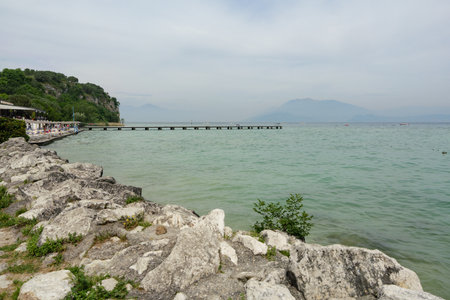 Rocky Shoreline And Pier Extending Into Lake Garda in Sirmione, Italy.の写真素材